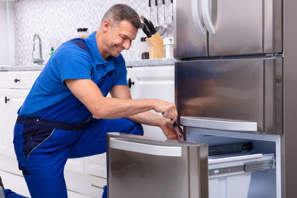 mature male serviceman repairing refrigerator with toolbox in kitchen
