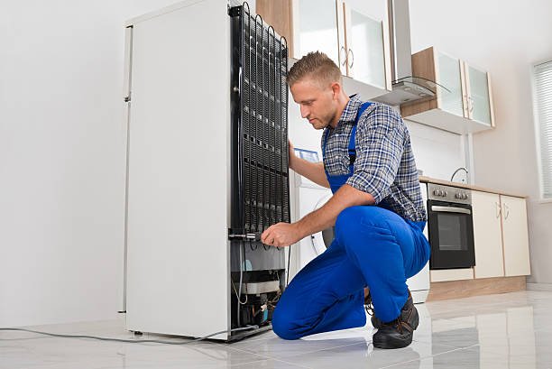 About male worker repairing refrigerator with screwdriver in house